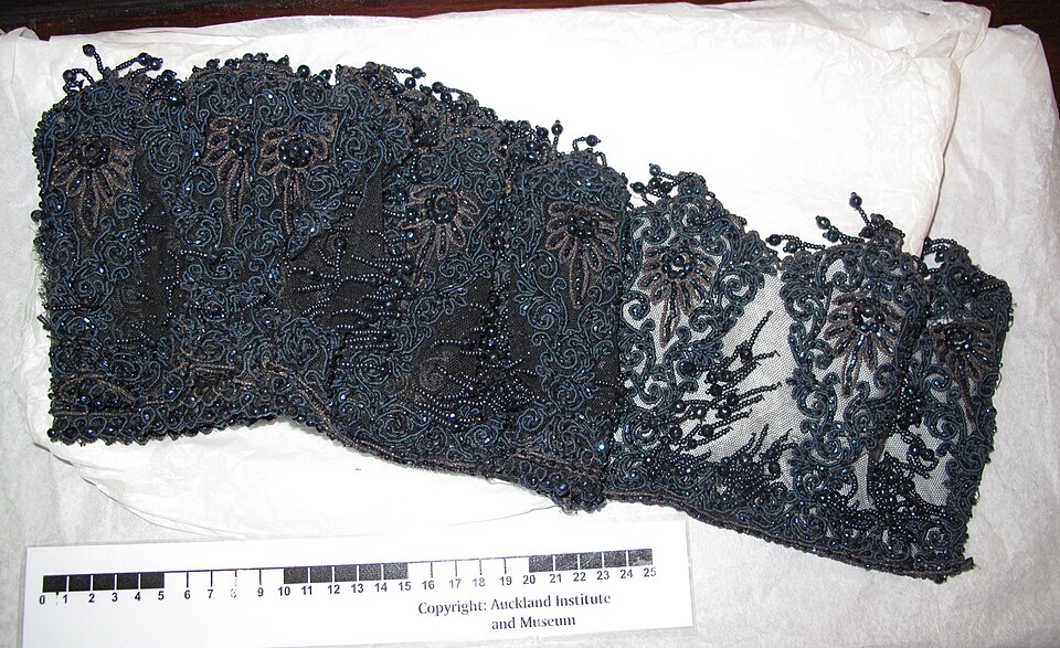 Real black beaded trimming laid flat beside a scale