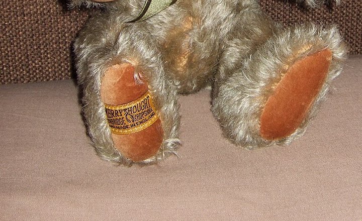 Close photograph of a gold and black Merrythought label stitched to a teddy bear paw pad